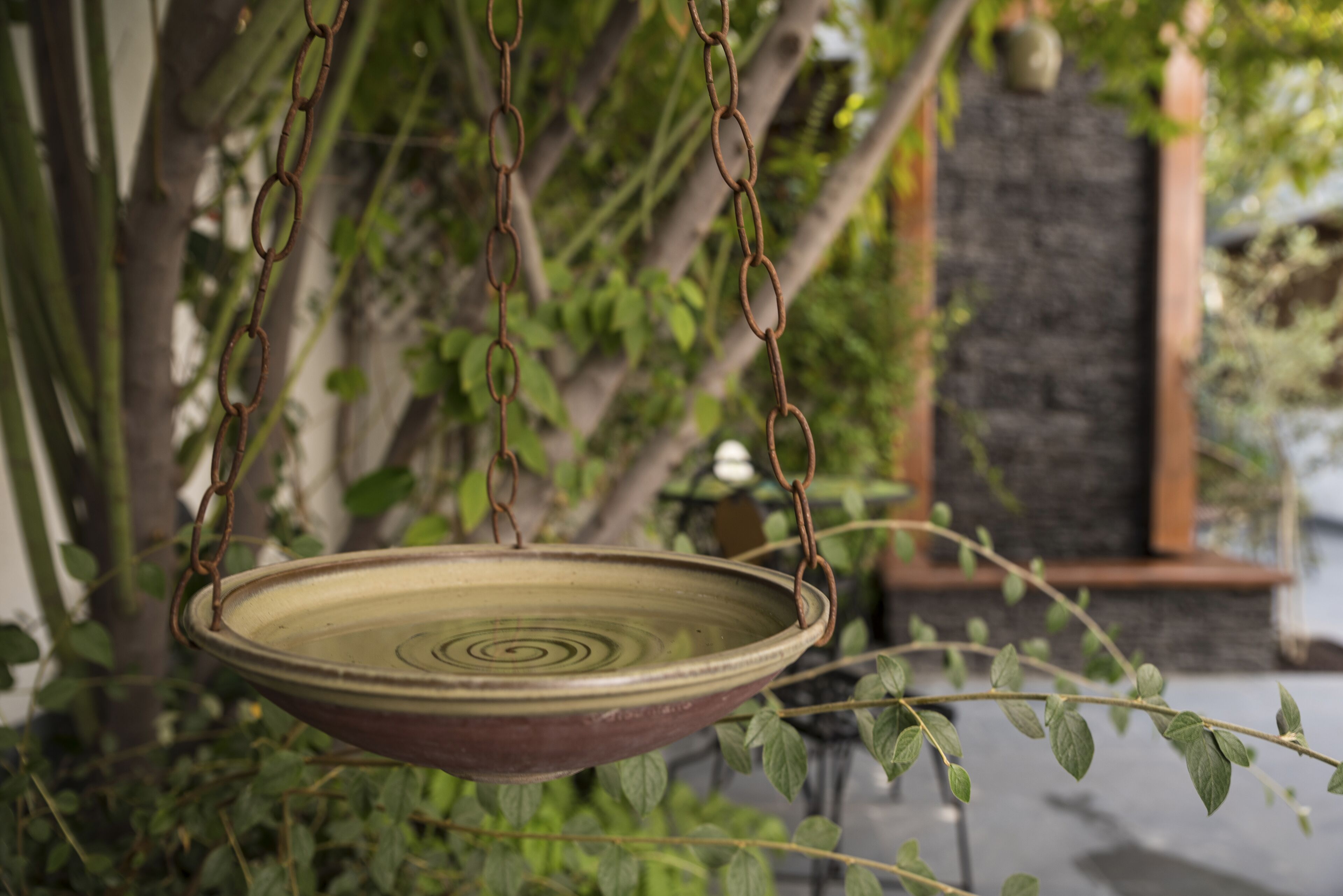 A hanging ceramic dish suspended by metal chains, surrounded by greenery.