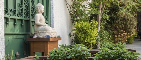 Eine Buddha-Statue auf einer Holzplattform vor einer grünen Tür mit schmiedeeisernem Dekor.