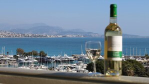 Eine Weinflasche und ein Glas auf einem Balkon mit Blick auf einen Yachthafen und eine Stadtlandschaft im Hintergrund.