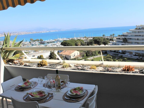 Balcón con mesa lista para comer, con vista a un puerto deportivo con barcos y un paisaje costero.