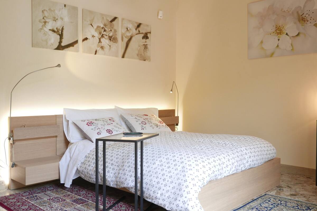 Ein Schlafzimmer mit einem Bett, Nachttischen, einer Lampe, einem Sessel und Bildern an den Wänden.