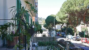 A street view with a building on the left, a tree-lined street, and parked cars. - Three Rooms (Messina)