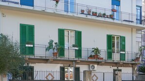 A multi-story building with balconies, green shutters, and potted plants. - Three Rooms (Messina)