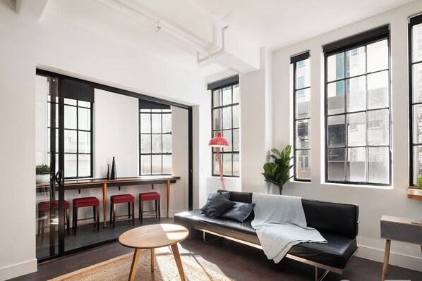 A modern living room with a black sofa, red bar stools, a wooden coffee table, and large windows with black frames.