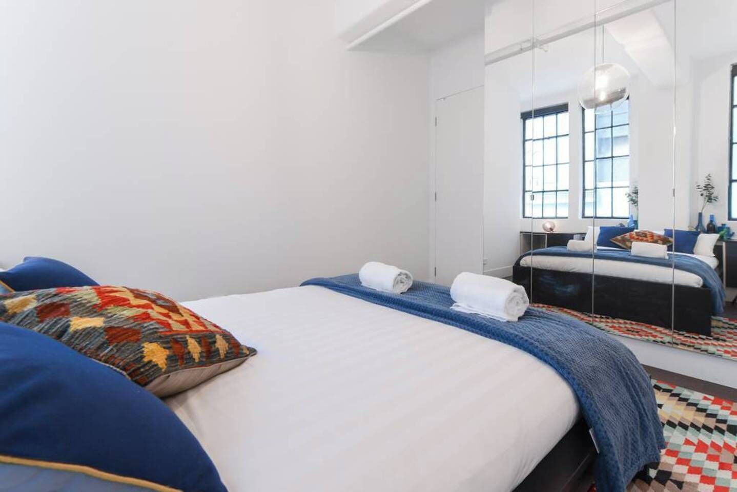 Ein modernes Schlafzimmer mit einem großen Bett, einem Spiegel und Blick auf die Stadt durch große Fenster.