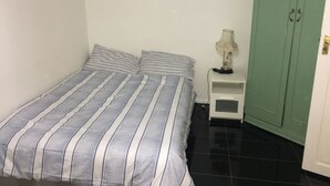 A bedroom with a bed, a nightstand, a lamp, and a green wardrobe. - Terraced house available for holiday vacation (London)