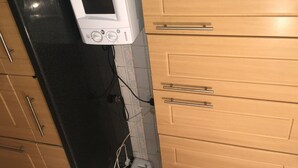 A kitchen with a white microwave, black countertop, and wooden cabinets with metal handles. - Terraced house available for holiday vacation (London)