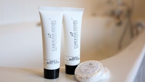 Dos tubos de jabón líquido para cabello y cuerpo Caroline Henry y una pastilla de jabón sobre una encimera de baño.
