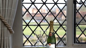 Una botella de champán Taittinger y dos copas en un alféizar con vistas a un campo verde y edificios.