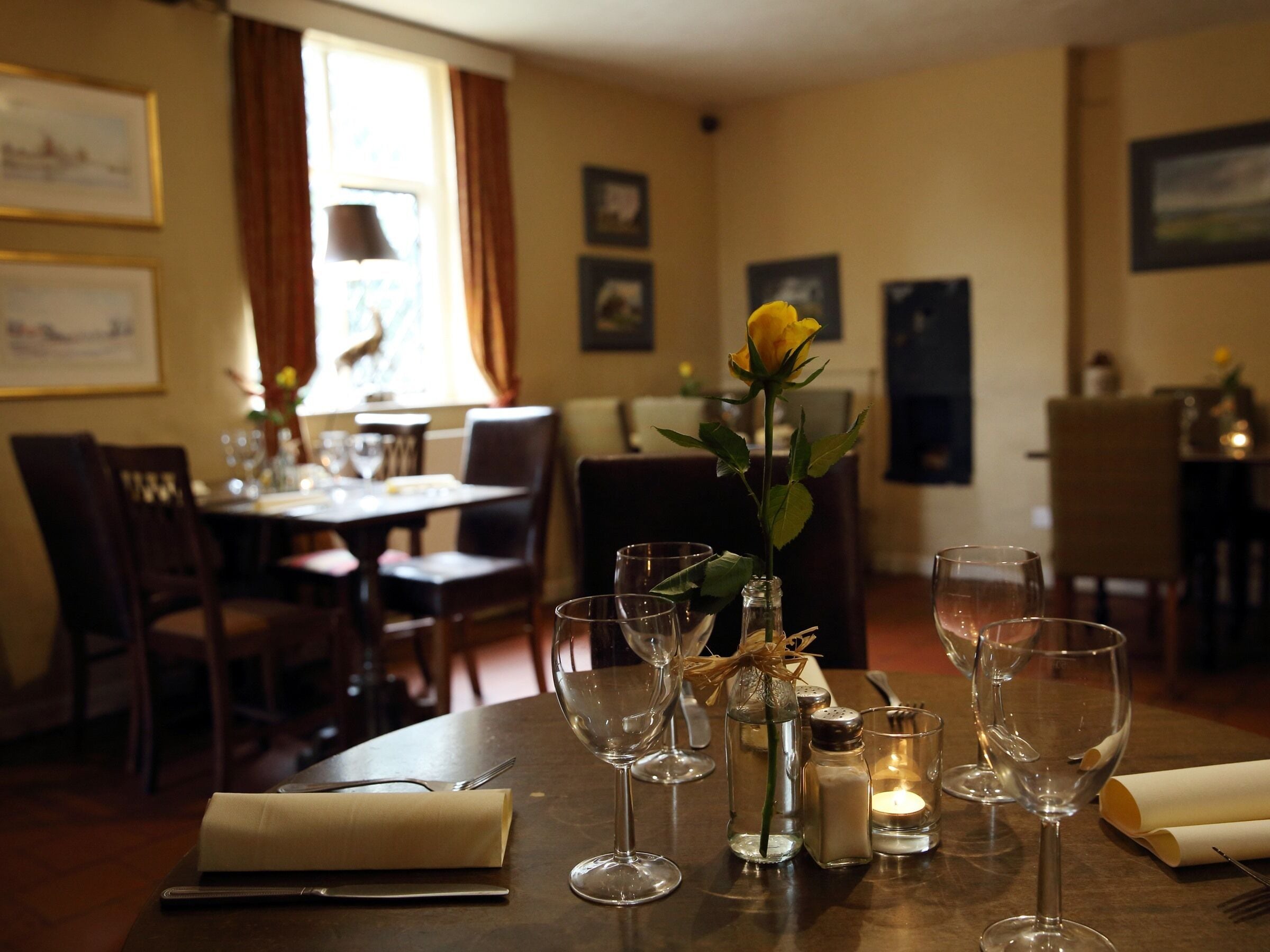 A dining table set with wine glasses, a candle, salt and pepper shakers, and a vase with a single yellow rose.