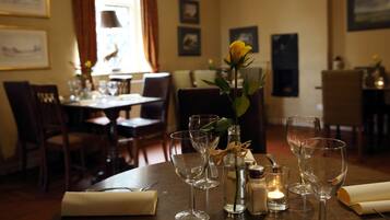 A dining table set with wine glasses, a candle, salt and pepper shakers, and a vase with a single yellow rose.