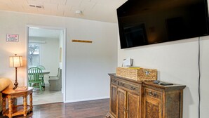 Ein Zimmer mit einem Holzkabinett, einem an der Wand montierten Fernseher, einer Lampe und einem Essbereich mit Stühlen und Tisch.
