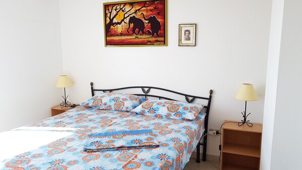A bedroom with a bed, two bedside tables, a lamp on each table, a painting above the bed, and a framed photo on the wall. - LUMINOUS SEA VIEWS IN SARDINIA, IDEAL FOR COUPLES OF FRIENDS AND FAMILIES! (Cala Gonone)