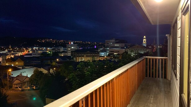 A balcony with a wooden railing overlooking a cityscape at night. - City House with harbour view! (Dunedin)