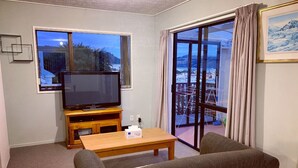 A living room with a television, a wooden coffee table, and two sofas. There is a large window with a view of a snowy landscape and a balcony. - City House with harbour view! (Dunedin)