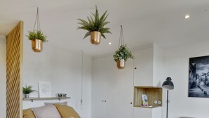 A modern bedroom with a bed, bedside tables, a desk, and a chair. There are plants hanging from the ceiling and a painting on the wall. - The Alcove Royale, furnished with 3 stars tourism (Versailles)