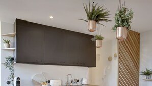 A modern kitchen with dark cabinets, a countertop, and hanging plants. - The Alcove Royale, furnished with 3 stars tourism (Versailles)