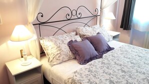 Un llit ben fet amb roba de llit estampada amb flors, dos almoinos i una tauleta de nit amb una làmpada.