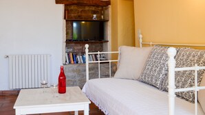 Une pièce chaleureuse avec un lit blanc, une petite table sur laquelle se trouvent une bouteille rouge et un verre, un téléviseur fixé à un mur en briques et une étagère en bois au-dessus du téléviseur.