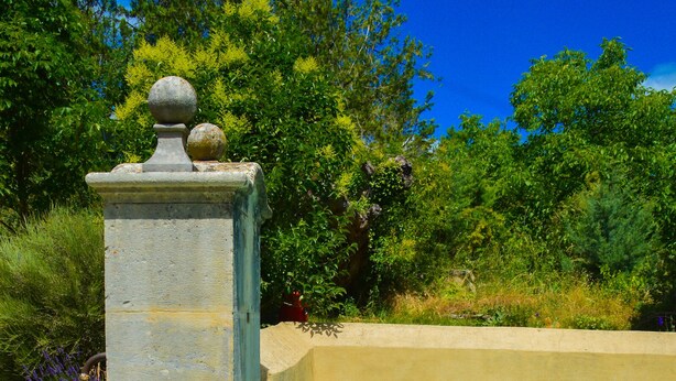 Une piscine à l’eau d’un bleu cristallin, entourée de verdure et bordée d’une structure en pierre surmontée d’une sphère.