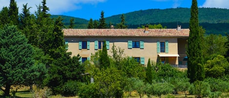 A two-story building with a tiled roof, surrounded by trees and a grassy field.