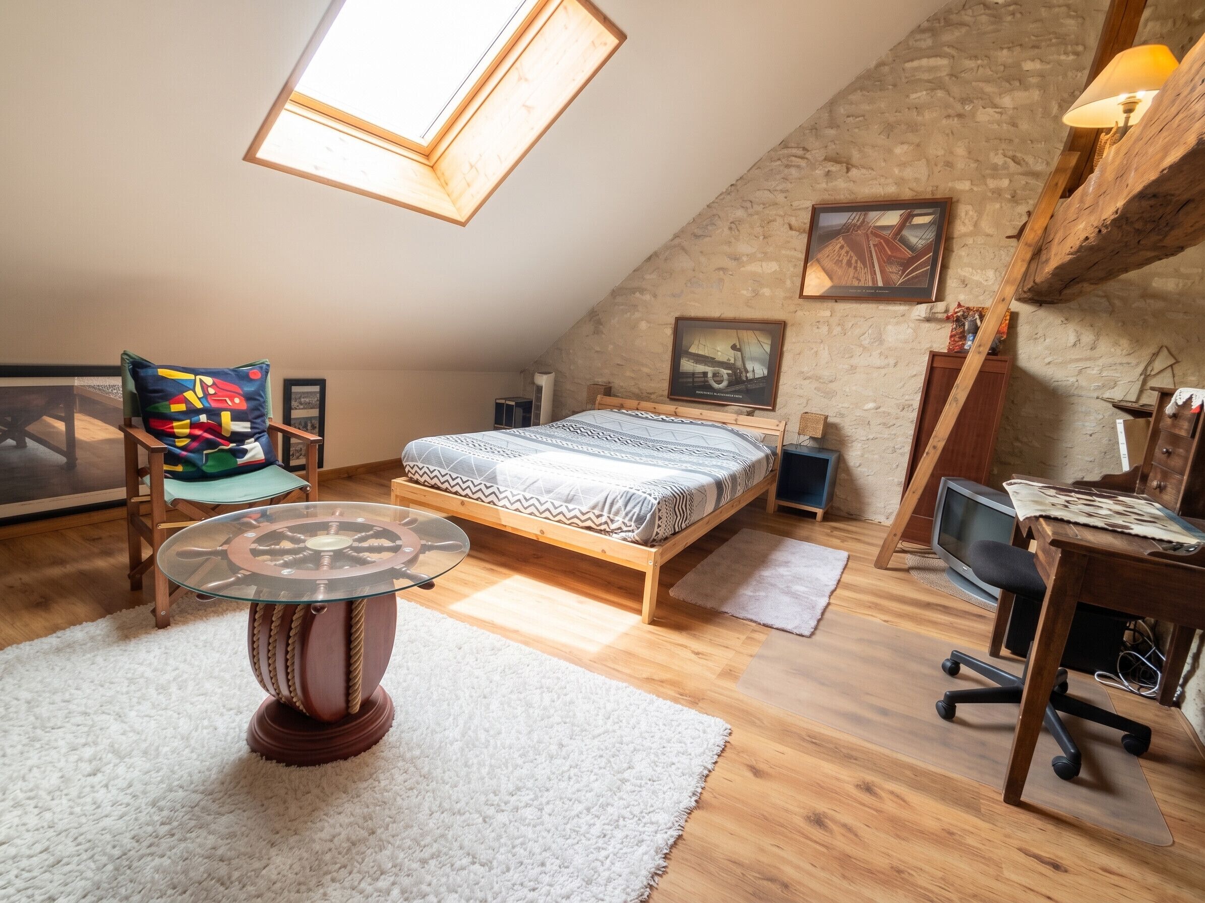 A loft bedroom with a sloped ceiling, a bed, a desk, a chair, a small table, and a window.