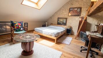 A loft bedroom with a sloped ceiling, a bed, a desk, a chair, a small table, and a window.