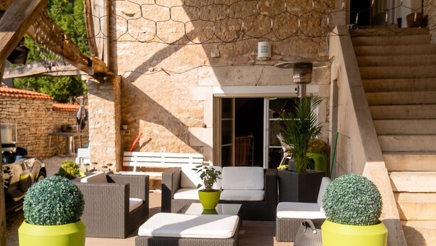 Une terrasse extérieure aménagée avec des meubles en osier, des plantes en pot et un mur en pierre.