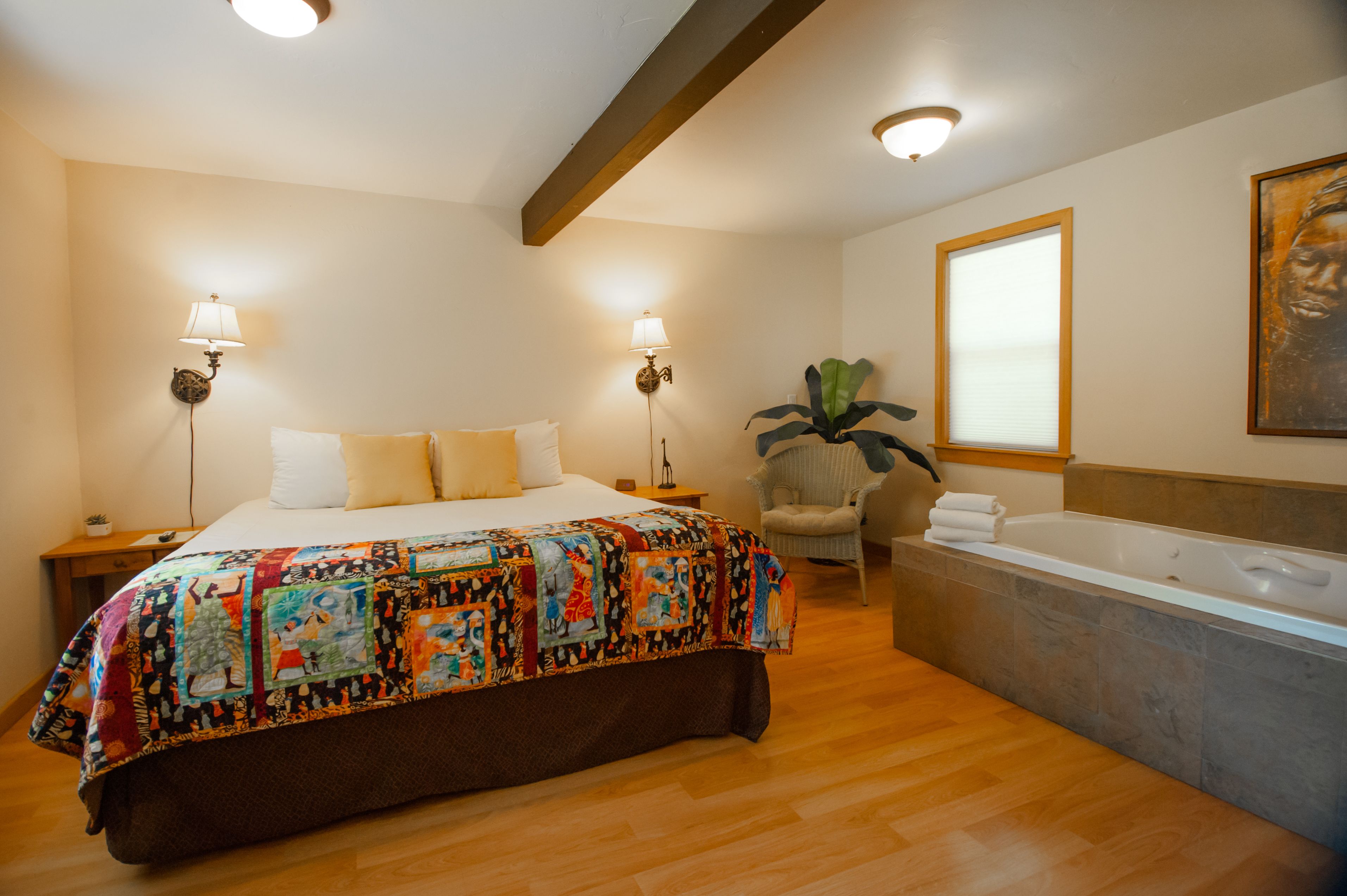 A bedroom with a large bed, two bedside lamps, a chair, a window, and a bathtub.