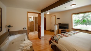 A hotel room with a large bed, a bathtub, a television, and a window with a view of trees. - The Islander Inn (Bigfork)