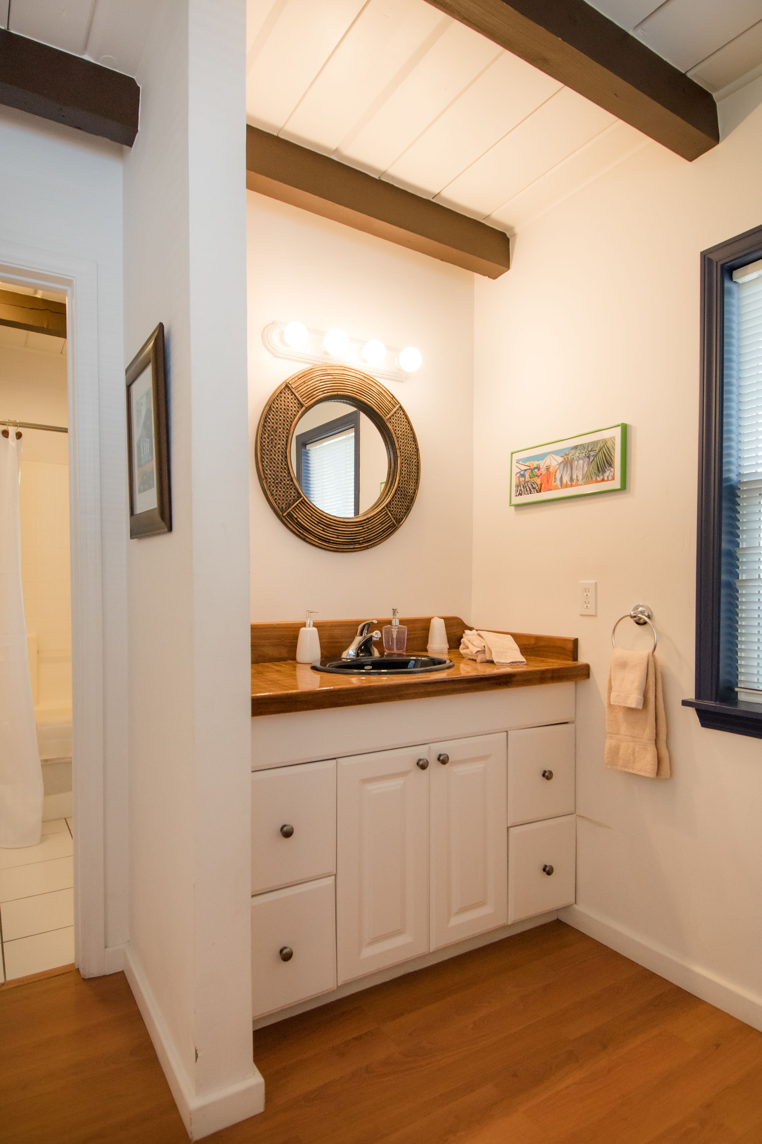 A bathroom with a wooden vanity, a mirror with lights, a towel rack, and a framed picture on the wall.