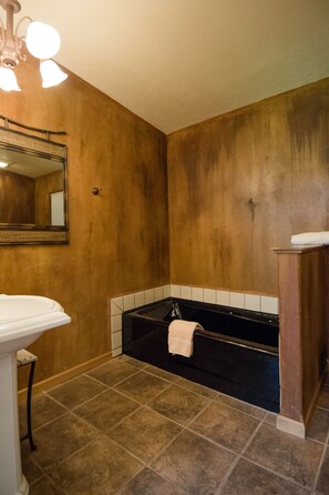 A bathroom with a wooden wall, a black bathtub, a white sink, and a mirror.