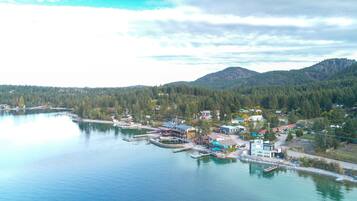 A lakeside town with docked boats, houses, and a forested hill in the background.
