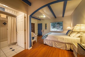 A bedroom with a bed, a window, and a bathroom with a shower and a toilet.