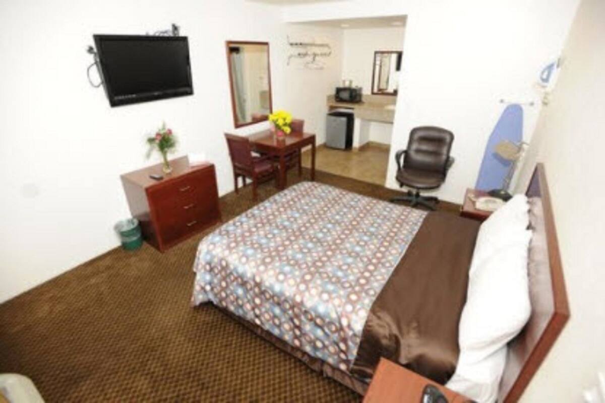 A hotel room with a bed, a desk, a chair, a television, and a small kitchenette.
