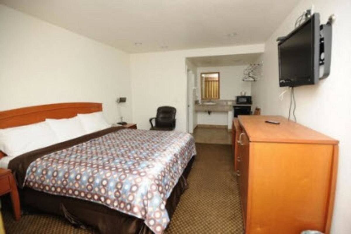 A hotel room with a bed, a desk, a chair, and a television.