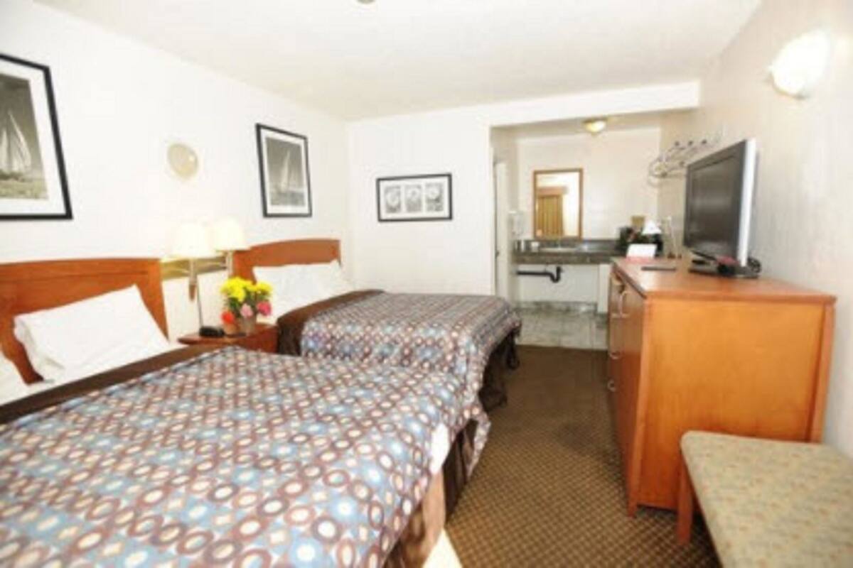 A hotel room with two beds, a desk, a television, and a small seating area.