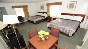 A hotel room with two beds, a desk with a lamp, a chair, and a small table with flowers. - Victoria Motel (Ventura)