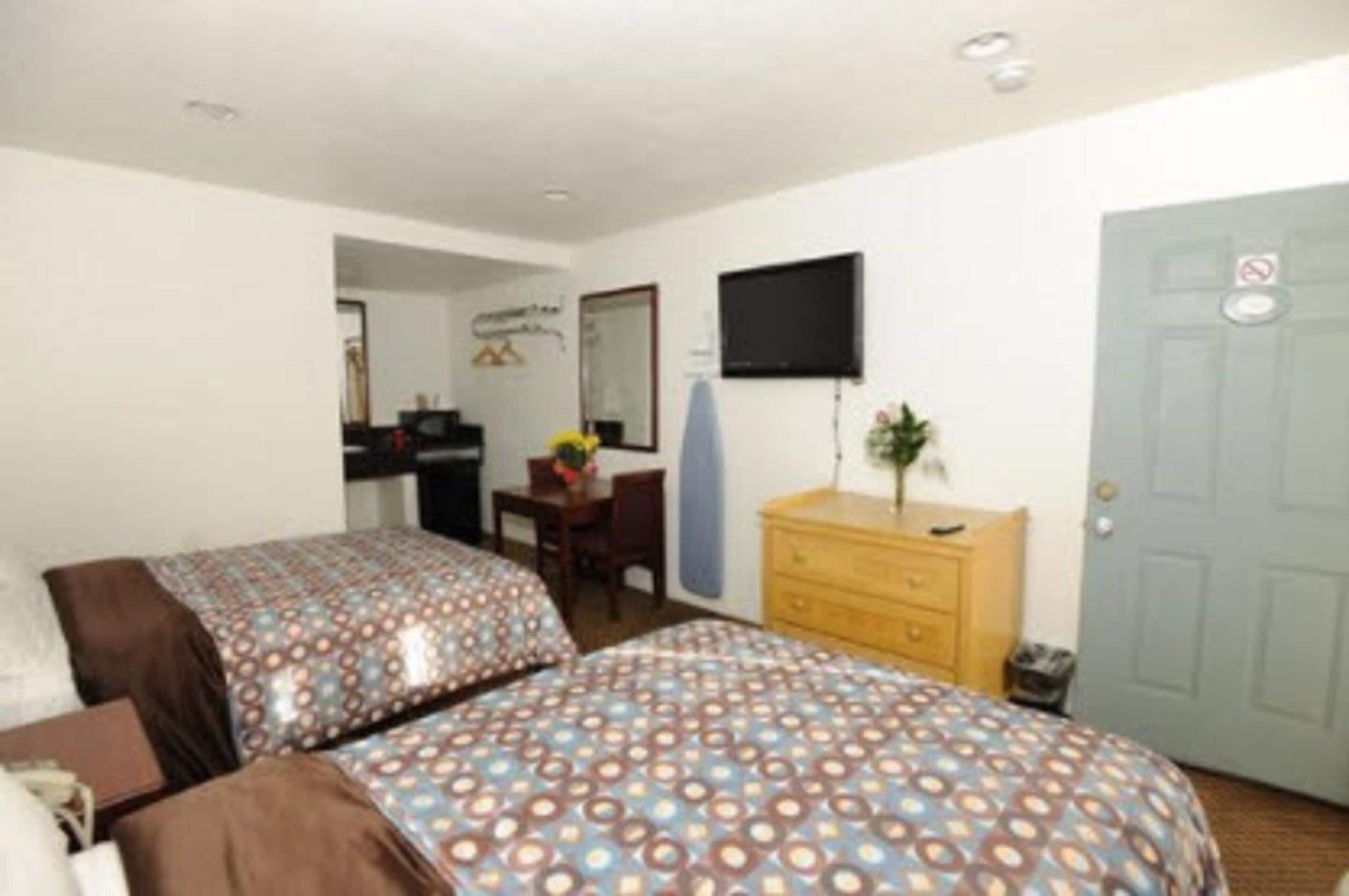 Una habitación con dos camas, un escritorio, un aparador, un televisor y una puerta.