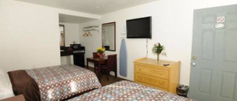 Una habitación con dos camas, un escritorio, un aparador, un televisor y una puerta.