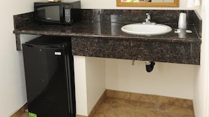 A compact bathroom with a sink, mirror, and a microwave on the countertop. - Victoria Motel (Ventura)