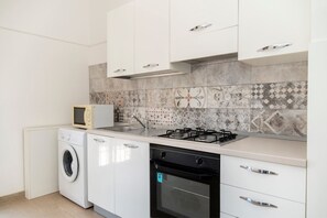 Une cuisine avec des meubles blancs, un four à micro-ondes, un lave-linge, une cuisinière à gaz et un lave-vaisselle.