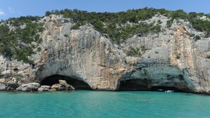 A coastal cave entrance with turquoise water, surrounded by rocky cliffs and greenery.