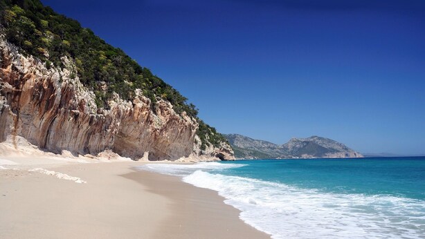 A beach with a rocky cliff and clear blue water.
