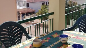 A balcony with a table set for two, chairs, and a view of the sea and buildings.