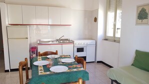 A compact kitchen with a dining table set for two, a refrigerator, a stove, and a sink.