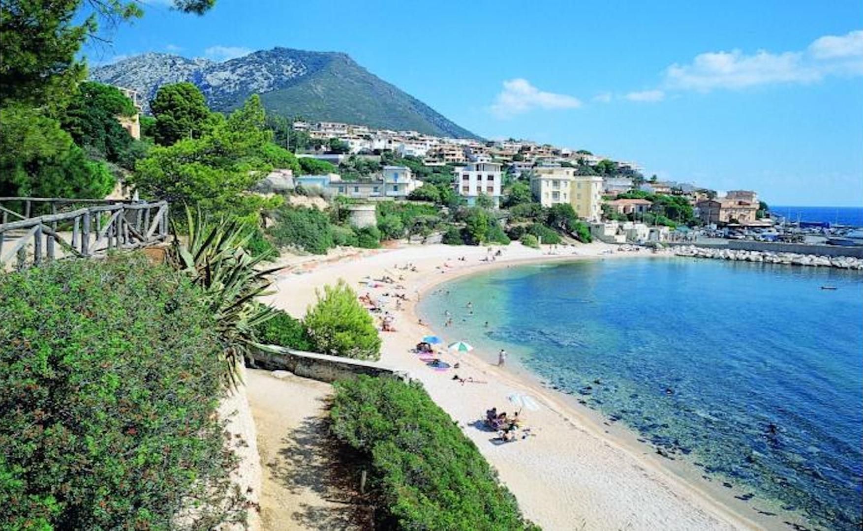 A coastal town with a beach, clear blue waters, and buildings on a hillside.