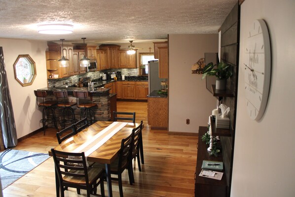A kitchen with wooden cabinets, a dining table with chairs, and a clock on the wall. - Elk from the Hot Tub - Bugle Inn (Weedville)