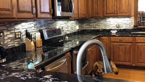 Una cocina con armarios de madera, un microondas de acero inoxidable y una encimera de mármol.