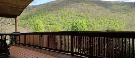 A wooden deck with a railing, overlooking a forested hillside.